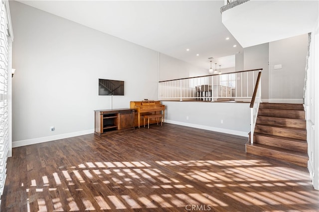 unfurnished living room with dark wood-type flooring, a towering ceiling, and a chandelier