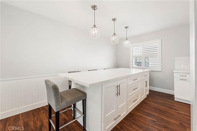 kitchen with a breakfast bar area, dark hardwood / wood-style floors, a kitchen island, pendant lighting, and white cabinets