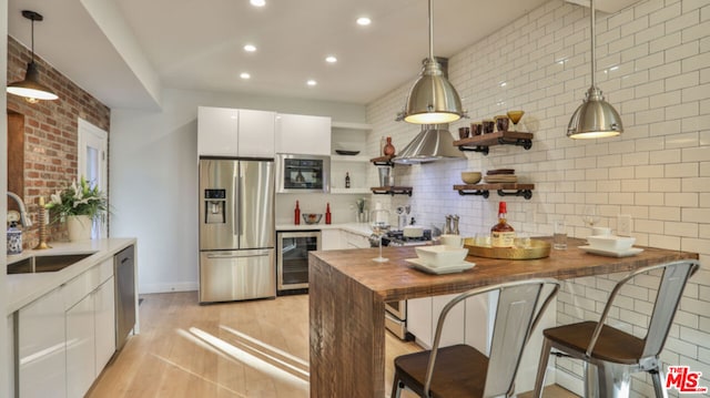 kitchen with appliances with stainless steel finishes, wood counters, sink, white cabinets, and hanging light fixtures