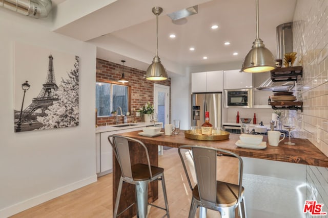 kitchen with stainless steel refrigerator with ice dispenser, butcher block counters, sink, pendant lighting, and white cabinets