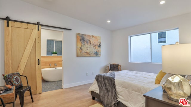 bedroom with lofted ceiling, light hardwood / wood-style floors, a barn door, and ensuite bathroom