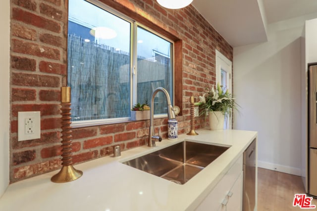 kitchen featuring white cabinetry, wood-type flooring, brick wall, and sink