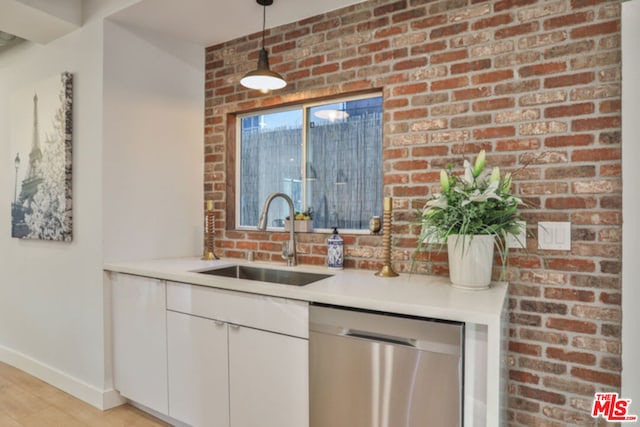 kitchen featuring brick wall, decorative light fixtures, white cabinetry, dishwasher, and sink