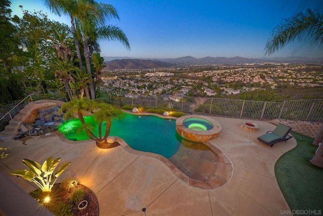 pool at dusk featuring a mountain view, a patio, and an in ground hot tub