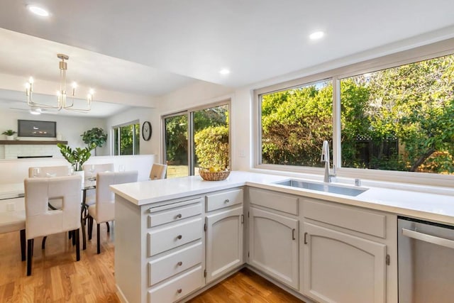 kitchen featuring sink, hanging light fixtures, light wood-type flooring, kitchen peninsula, and dishwasher