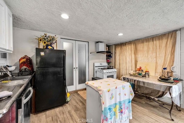 kitchen with black fridge, white gas range oven, white cabinets, light hardwood / wood-style floors, and wall chimney range hood