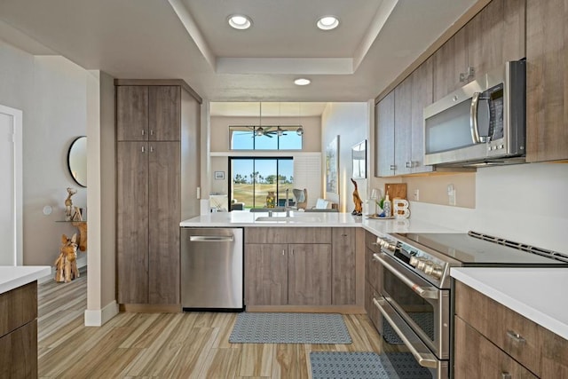 kitchen featuring sink, light wood-type flooring, a tray ceiling, stainless steel appliances, and an inviting chandelier