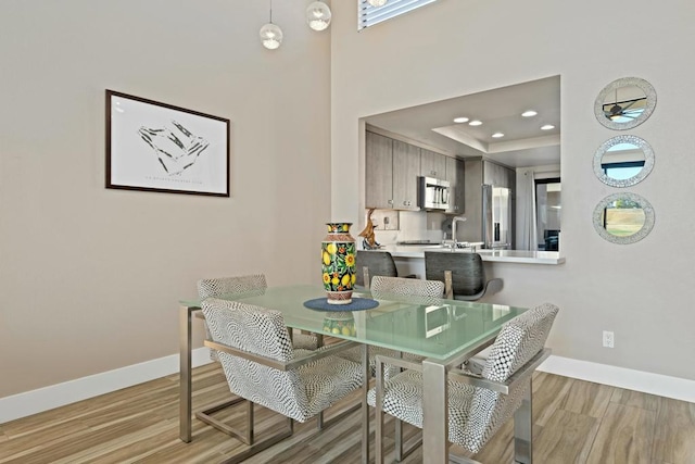 dining area with a raised ceiling and light wood-type flooring