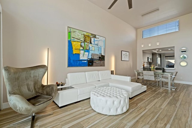 living room featuring a high ceiling, ceiling fan, and light hardwood / wood-style floors