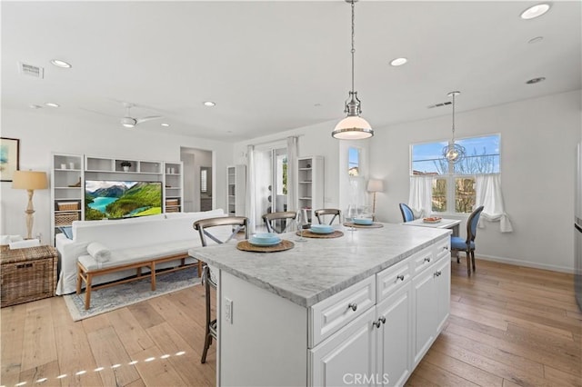 kitchen with white cabinetry, a center island, hanging light fixtures, and light hardwood / wood-style flooring