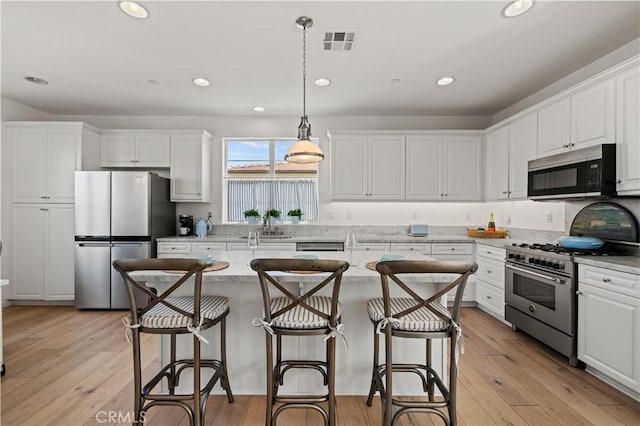 kitchen with stainless steel appliances, hanging light fixtures, white cabinets, and light stone counters