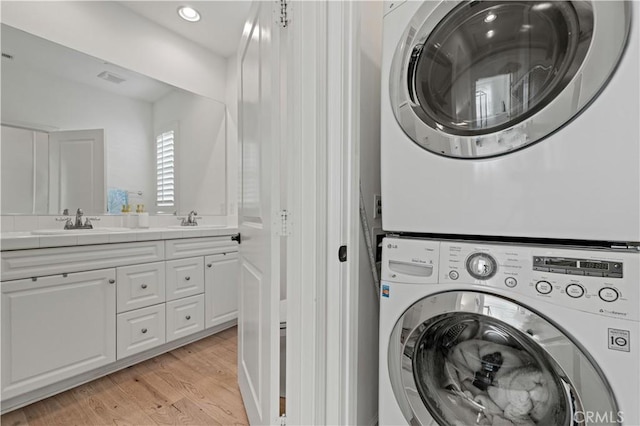 laundry area featuring stacked washer / dryer, sink, and light hardwood / wood-style floors