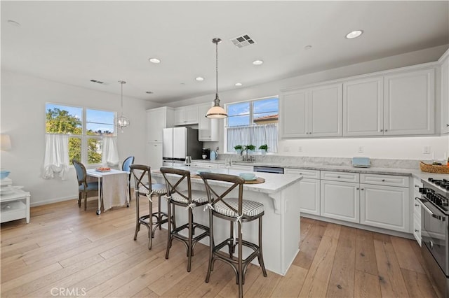 kitchen featuring white cabinetry, a center island, appliances with stainless steel finishes, pendant lighting, and light stone countertops