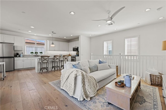 living room featuring ceiling fan, sink, and light hardwood / wood-style flooring