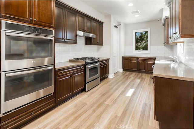 kitchen featuring dark brown cabinetry, sink, light wood-type flooring, stainless steel appliances, and backsplash