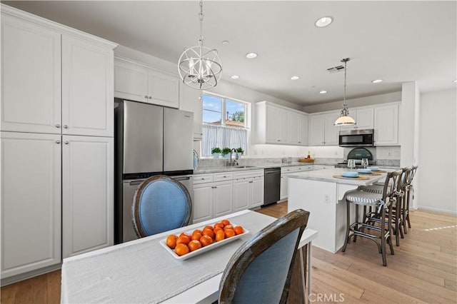 kitchen featuring decorative light fixtures, stainless steel appliances, white cabinets, and a kitchen island