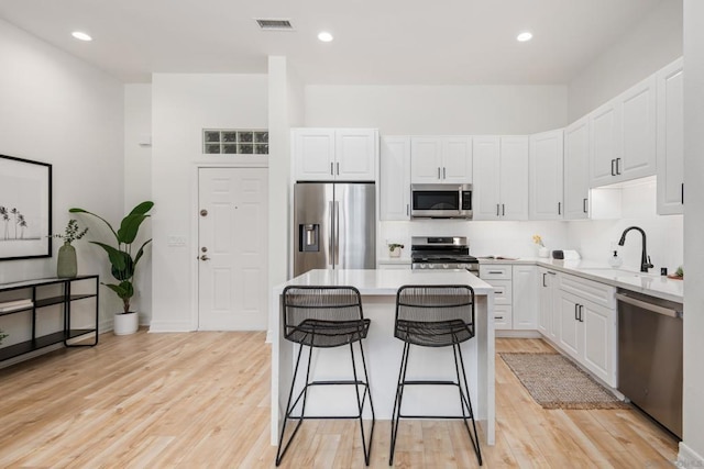 kitchen with sink, a breakfast bar area, a kitchen island, stainless steel appliances, and white cabinets