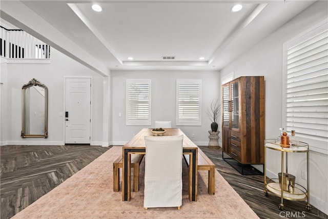 dining area featuring a raised ceiling, plenty of natural light, and dark parquet floors