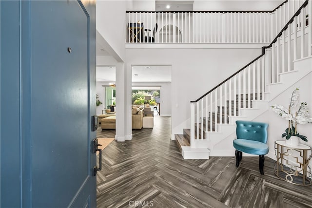 entryway with a towering ceiling and dark parquet flooring