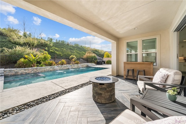 view of pool with pool water feature, an outdoor fire pit, exterior bar, and a patio