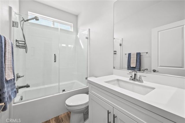 full bathroom featuring hardwood / wood-style flooring, vanity, shower / bath combination with glass door, and toilet