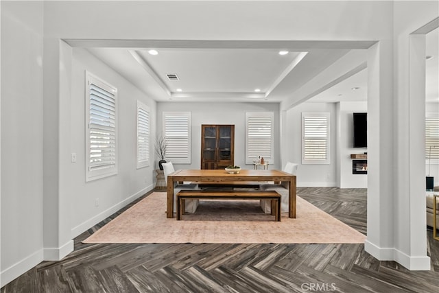 dining space with dark parquet flooring and a tray ceiling