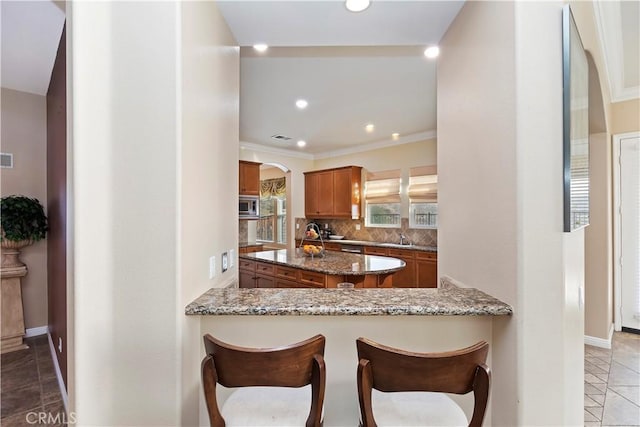 kitchen featuring stainless steel microwave, backsplash, dark stone counters, light tile patterned floors, and kitchen peninsula