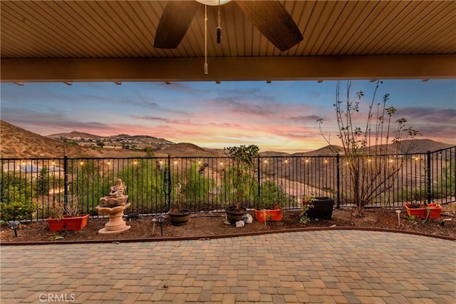 patio terrace at dusk featuring ceiling fan and a mountain view