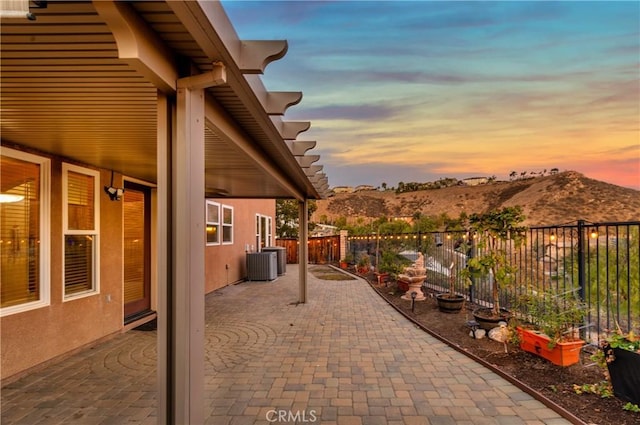 patio terrace at dusk featuring central AC unit and a mountain view