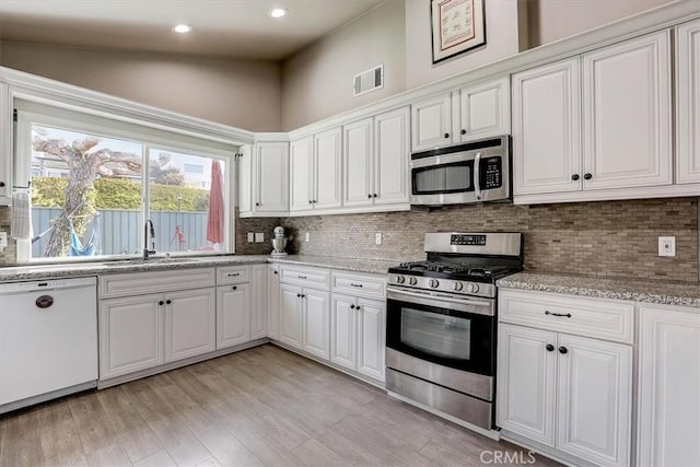 kitchen with appliances with stainless steel finishes, tasteful backsplash, white cabinetry, sink, and light hardwood / wood-style floors