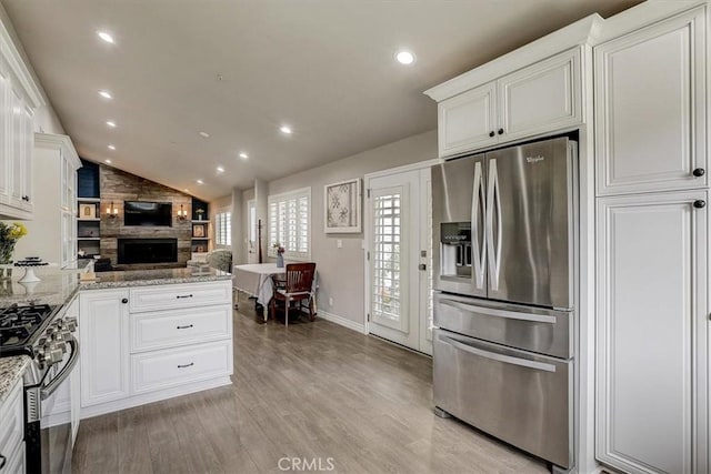 kitchen with lofted ceiling, white cabinetry, light wood-type flooring, stainless steel appliances, and light stone countertops