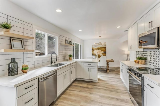 kitchen featuring appliances with stainless steel finishes, pendant lighting, sink, white cabinets, and light hardwood / wood-style flooring