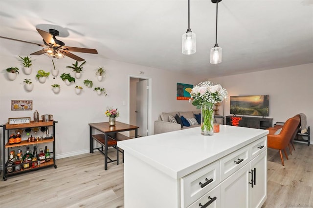 kitchen with ceiling fan, white cabinetry, hanging light fixtures, a center island, and light hardwood / wood-style floors