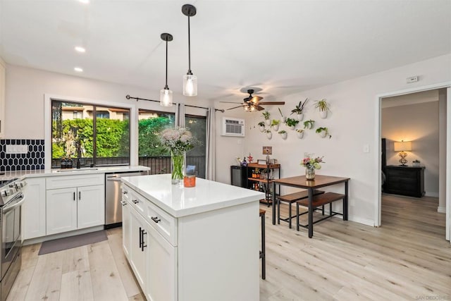 kitchen with hanging light fixtures, stainless steel appliances, a center island, white cabinets, and light wood-type flooring