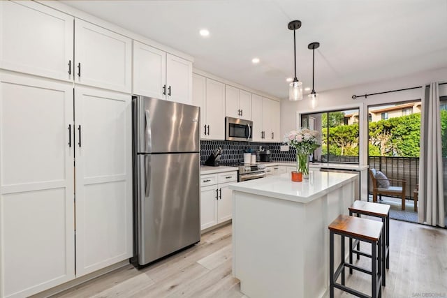 kitchen with pendant lighting, appliances with stainless steel finishes, a kitchen breakfast bar, a center island, and white cabinets