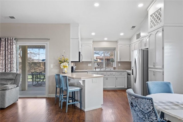 kitchen with a breakfast bar, dark hardwood / wood-style floors, stainless steel appliances, white cabinets, and tasteful backsplash