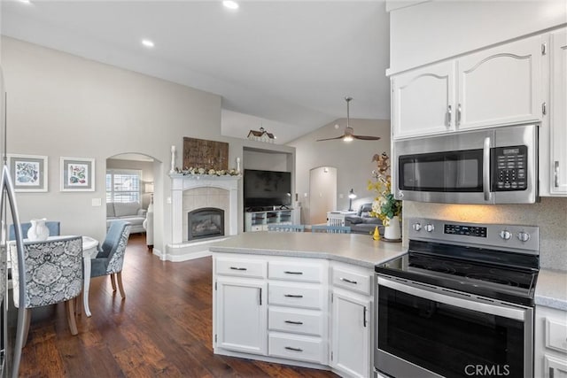 kitchen featuring white cabinetry, kitchen peninsula, lofted ceiling, stainless steel appliances, and a tile fireplace