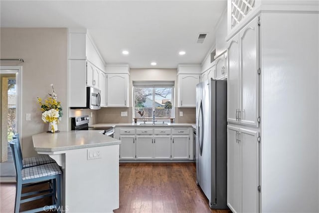 kitchen featuring white cabinetry, kitchen peninsula, dark wood-type flooring, appliances with stainless steel finishes, and a breakfast bar area