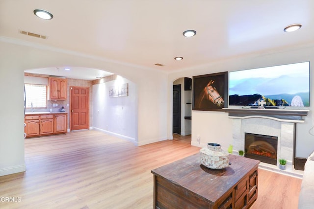 living room featuring crown molding, a high end fireplace, and light hardwood / wood-style flooring