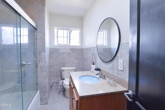 full bathroom with vanity, combined bath / shower with glass door, tile walls, and toilet