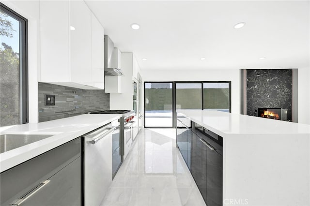 kitchen featuring white cabinetry, a wealth of natural light, wall chimney range hood, and a fireplace