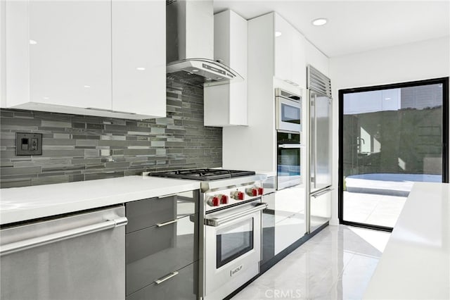 kitchen with tasteful backsplash, wall chimney exhaust hood, stainless steel appliances, and white cabinets