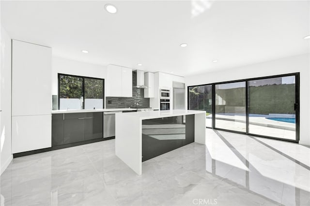 kitchen with a kitchen island, white cabinets, backsplash, stainless steel appliances, and wall chimney exhaust hood