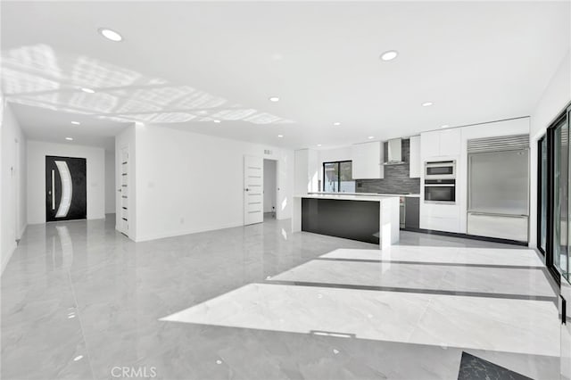 kitchen with a center island, built in appliances, white cabinets, decorative backsplash, and wall chimney exhaust hood