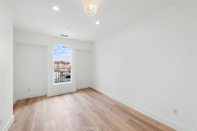 spare room featuring a chandelier and light hardwood / wood-style floors