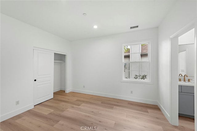 unfurnished bedroom with ensuite bathroom, sink, light wood-type flooring, and a closet