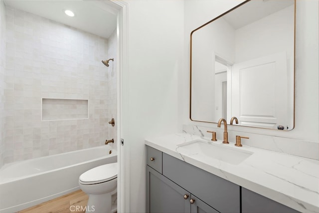 full bathroom with hardwood / wood-style flooring, tiled shower / bath, vanity, and toilet