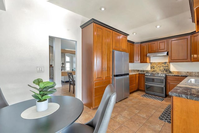 kitchen featuring sink, light tile patterned floors, dark stone countertops, stainless steel appliances, and backsplash