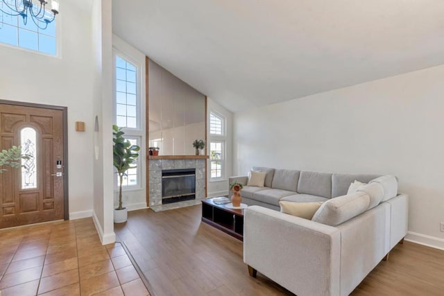 living room featuring wood-type flooring, high vaulted ceiling, a tile fireplace, and a notable chandelier