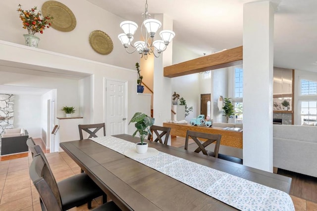 dining room with an inviting chandelier, high vaulted ceiling, a tile fireplace, and light tile patterned floors